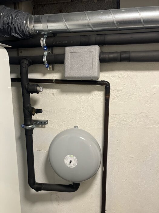 Rörsystem i källare med grå expansionstank och metallrör.