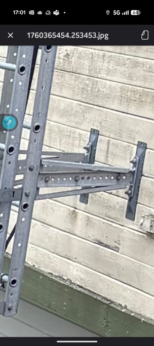 Metallkonsoler fastsatta på en vägg med träpanel, med många hål för skruvar längs konsolerna.