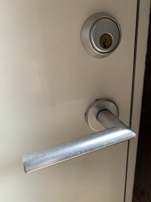 Löst dörrhandtag med ett litet hål i brickan, synlig cylinderlås, vitt dörrblad.