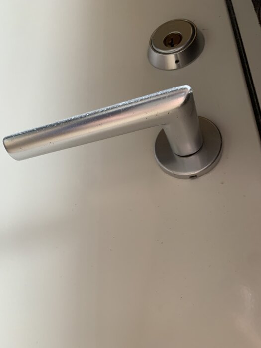 Löst dörrhandtag med ett litet hål i brickan, monterat på en dörr.