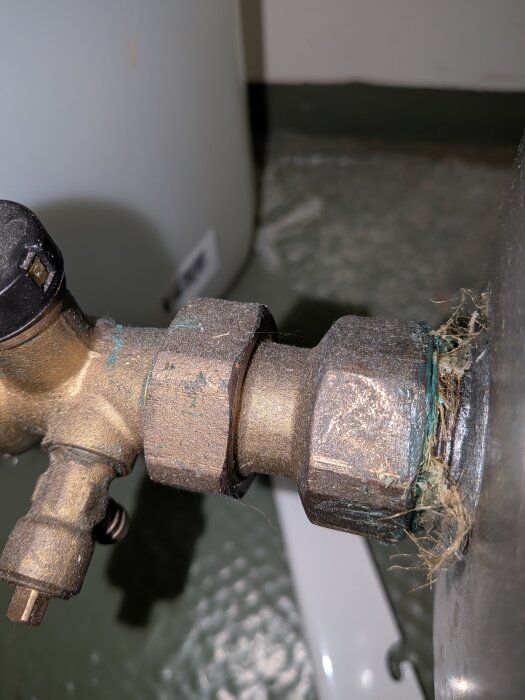 Ventil med metallgänga och mutter, omgiven av grönt oxiderat material och tätningsfiber i närbild.