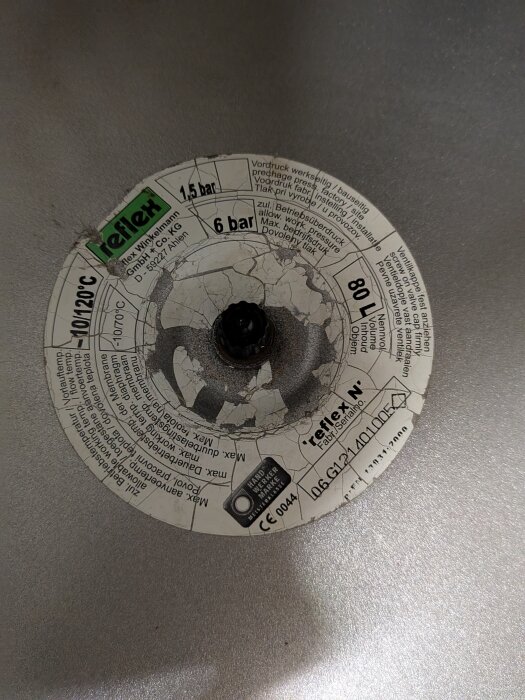 En trasig etikett på en Reflex-expansionskärl med specificerade tryckvärden och en rostig, centrerad mutter.