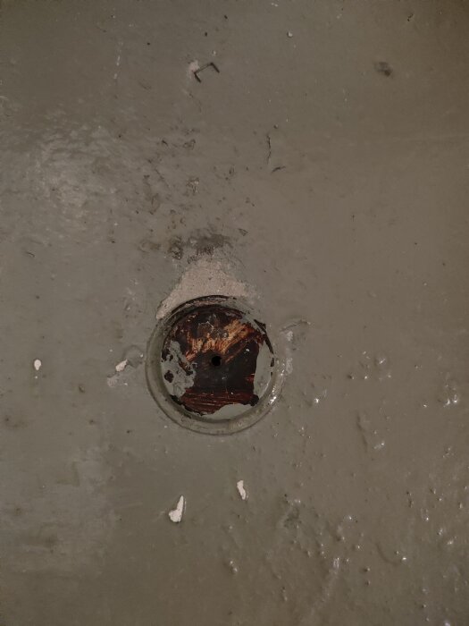 Rostig rund platta på golv, oklart om det är ett avloppsrör eller luftningsuttag.