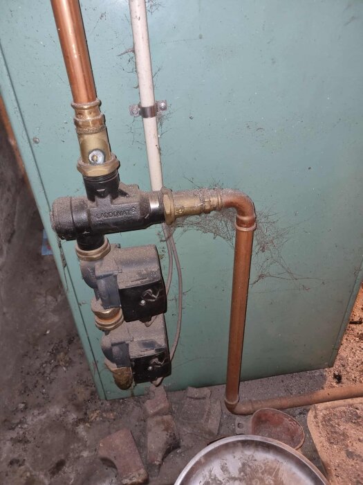 Närbild på en gammal vattenrörsinstallation med ventiler och kopparrör mot en dammig vägg.