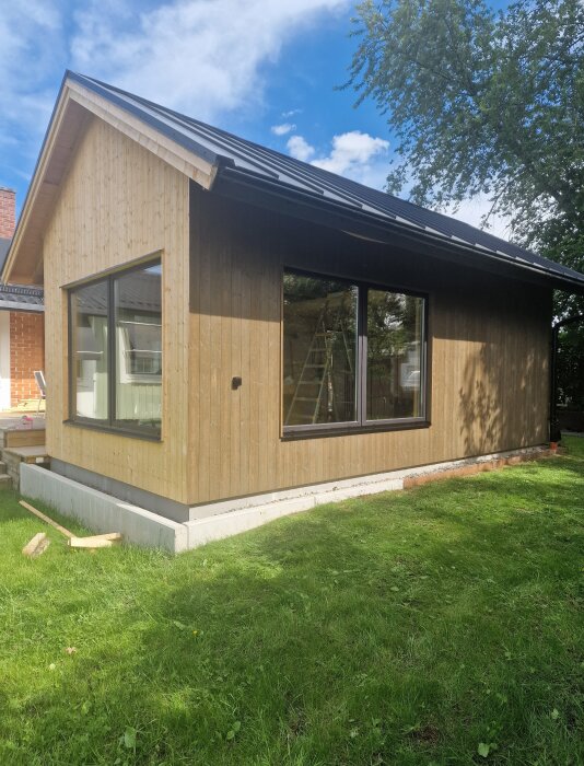 Nymålat hus med tjärvitrol och svarta detaljer som hängrännor och fönster, omgiven av gräsmatta och träd.