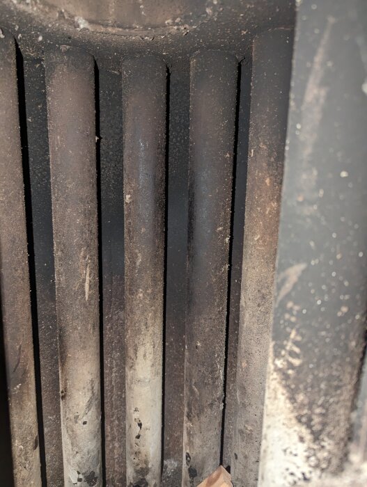 Kaminens insida med flera vertikala metallrör, sotiga och använda, eventuellt fördelaktiga för värmespridning i bastu.