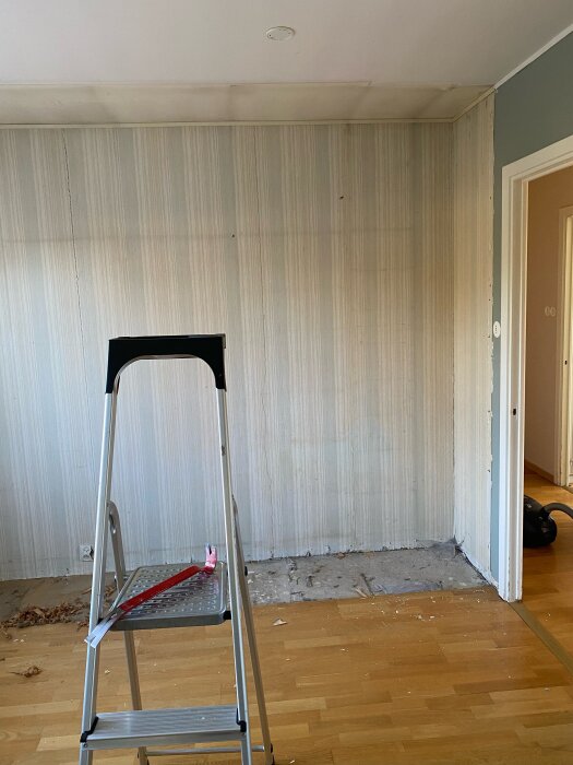 Tom plats där en garderob stått, med synlig betongplatta och parkettgolv runtom, en stege och verktyg vid sidan av väggen.