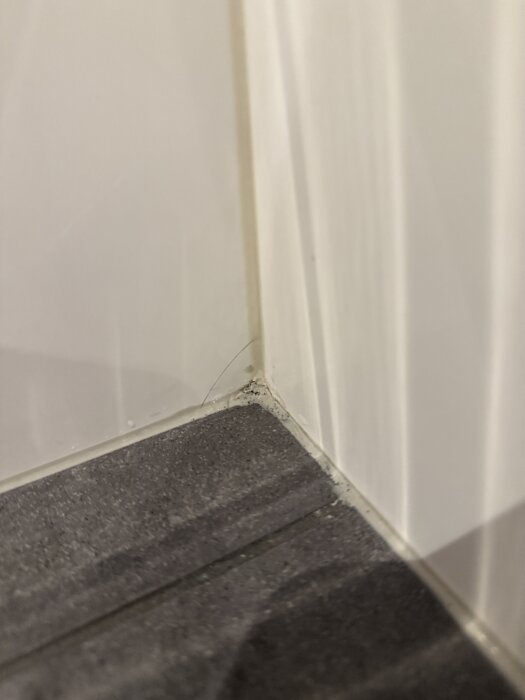 Sprucket kakel i duschhörn med mörka prickar på silikonfogen.