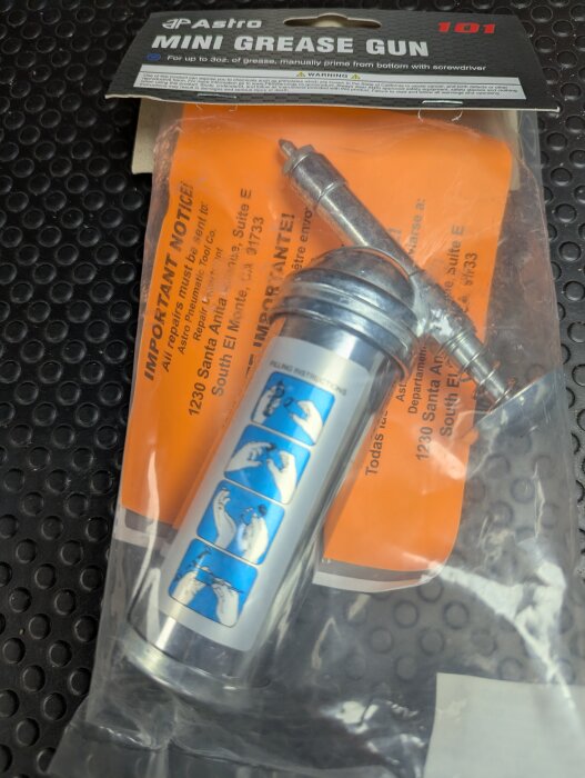 Mini fettspruta i förpackning med monteringsinstruktioner och orange bakgrund.