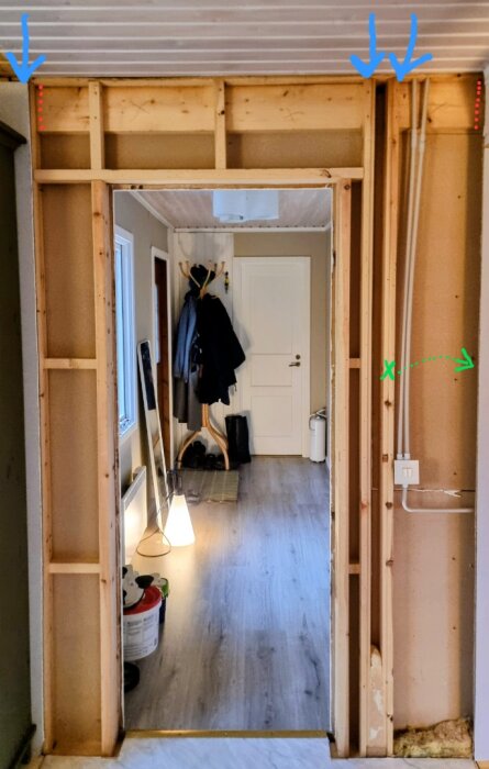 Öppen väggkonstruktion med träbalkar och blå pilar som markerar en sektion för potential utbyggnad av dörröppning.