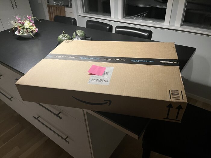 Stor Amazon Prime-låda på köksbänk med blombukett i bakgrunden.