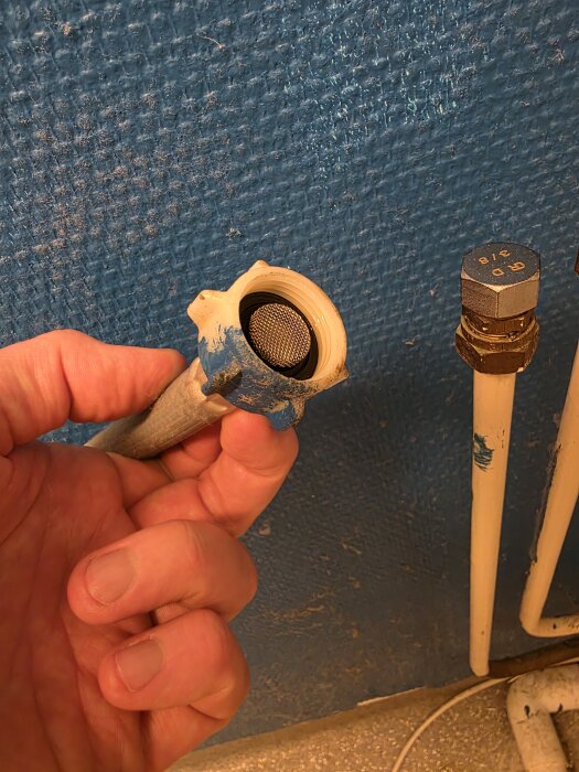 En person håller en tvättmaskinslang med plastkoppling framför en 15mm vattenledning på en blå vägg.