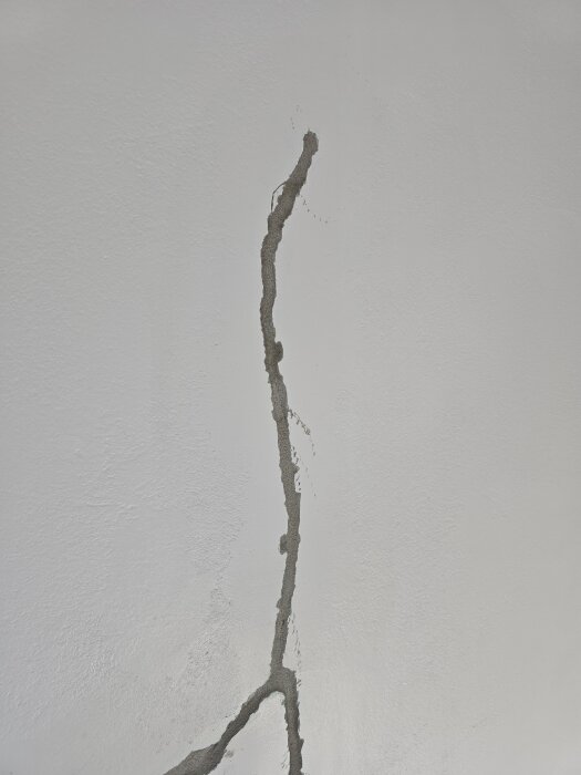 Spricka i en vit vägg fylld med torkat bruk, visar pågående renoveringsarbete.