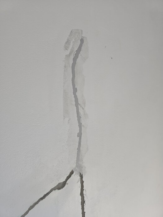 Sprucken vägg med torkande spackel synligt, en del av pågående renovering för att skapa en fondvägg i ett annars vitt rum.