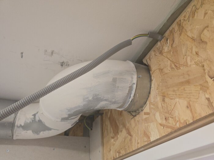 Flexibelt ventilationsrör i ett rum under renovering med synlig dragning av elrör ovanför spacklad vägg.