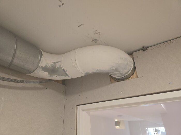 Ventilationsrör monterat nära ett tak i ett rum under renovering. Rör och vägg är förberedda för att dra om el och installera nya takspottar.