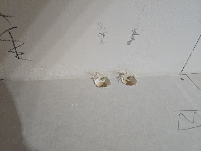 Två borrade hål i en vit vägg med ritade märkningar omkring, förberett för installation eller eldragning inom ett renoveringsprojekt.