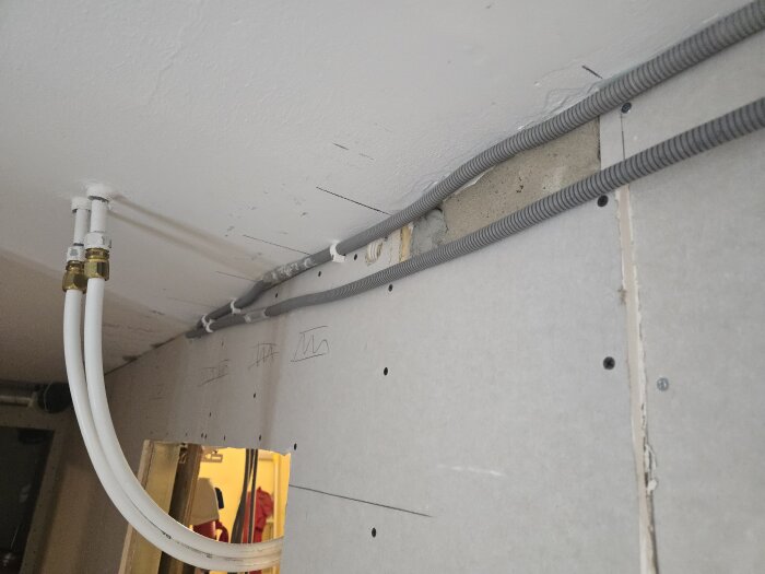 Elkablar och vattenrör installerade i väggen; flexrör dras från taket i byggprojekt.