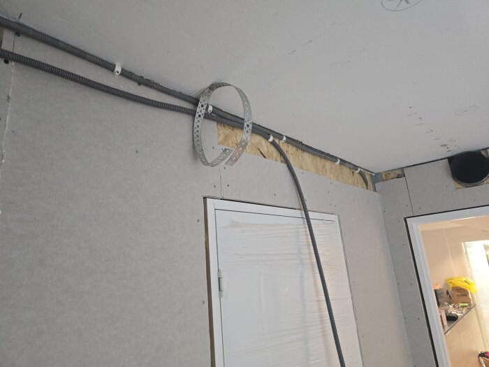 Vägg med installationsrör och kabelslang för eldragning, samt tak där takspottar planeras, i en renovering av en korridor.