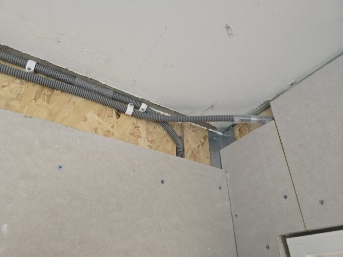 Elektriska flexrör monterade längs tak och vägg i ett rum under renovering, med spånskivor och gipsskivor synliga.