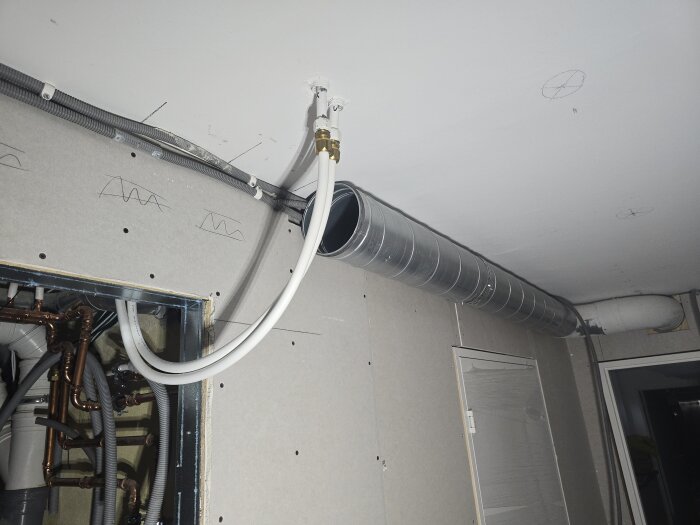 Ventilationsrör och elinstallation i ett halvfärdigt rum, synliga flexrör och kopparrör, tak och vägg under konstruktion.