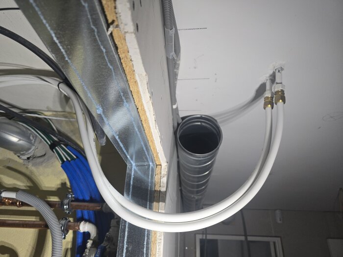 Takinstallation med flexrör och luftventilationsrör i ett rum under renovering. Kablar och rör är synliga vid en öppen struktur.