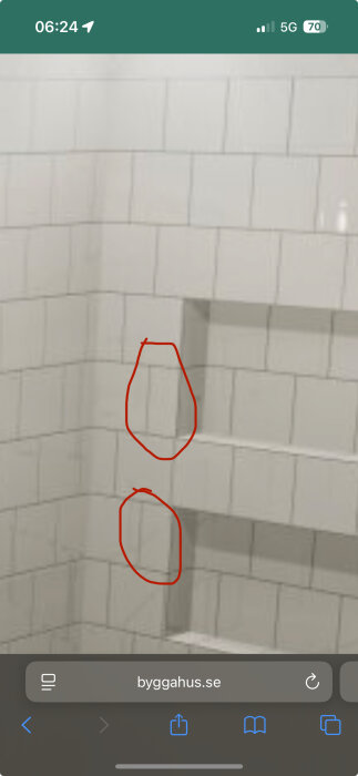 Vita kakelplattor på en vägg, två plattor inringade med röd markering, indikerar ojämn fogläggning på källartoalett.