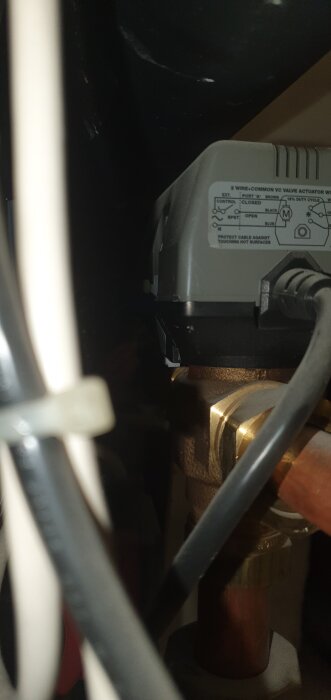 Bild av ventil med vit pigg i nedre läge, kopplad till rör och elektriska kablar, med etikett på ventilen.