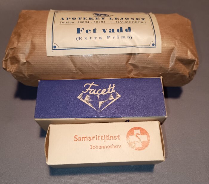 Förbandslåda innehållande paket med fetvadd från Apoteket Lejonet, en blå Facett-förpackning och en kartong från Samarittjänst Johanneshov.