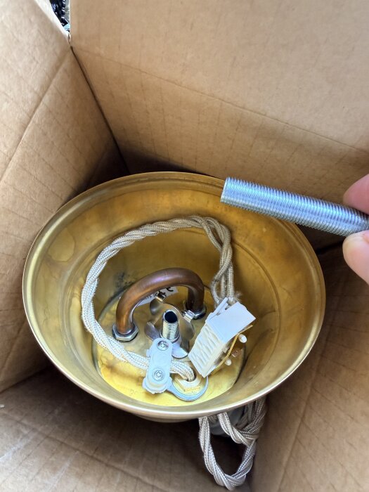 Kartong med kopplingsplint och kablar, möjligtvis en lampsockel, där jorden ansluter via plinten samt en silverfärgad rördetalj i handen.