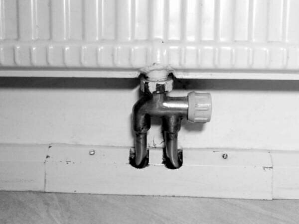 En radiatoranslutning med tvårörskoppel och bypass-inställning monterad under ett element.