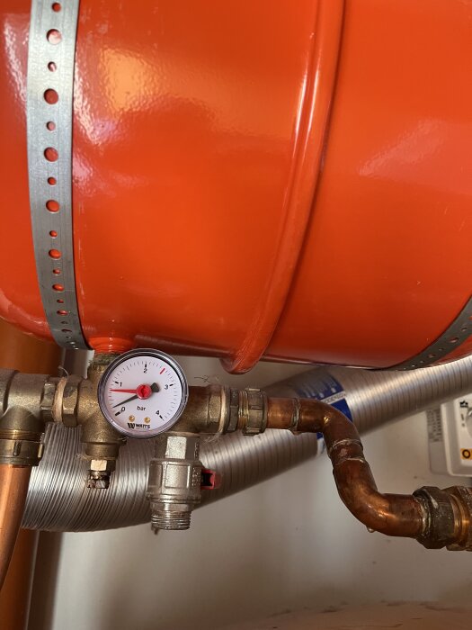 Manometer kopplad till ett orange expansionskärl, visare på samma position, omgiven av rör och ventil.