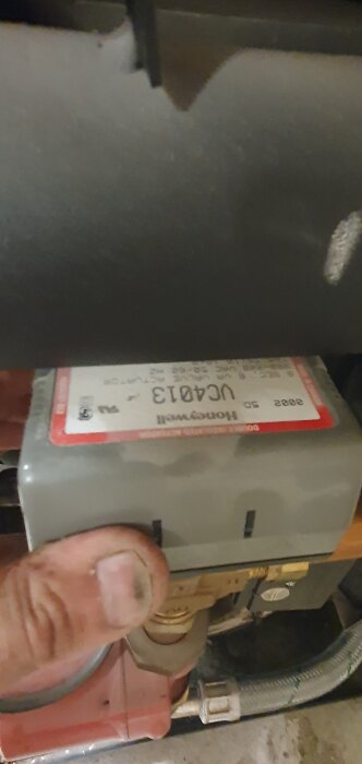 En person håller i ett ställdon från Honeywell, modellnummer VCA013, kopplat till rörsystem under installation eller reparation.