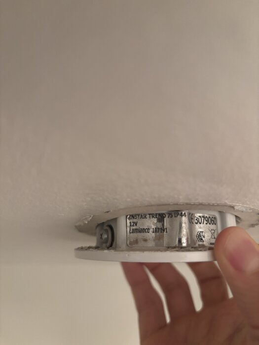 Spotlight i taket med märkning "InStar Trend 75 IP44" och handen som håller den. Modellen är Lumience 079060.