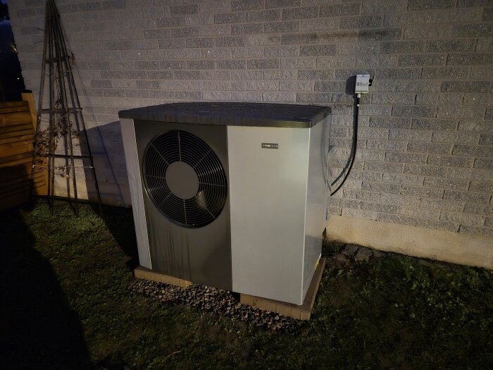 Utedel av värmepump Nibe S2125 installerad nära tegelvägg, står på betongplatta nära marknivå, med ansluten elbox.