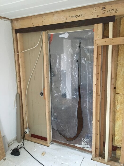 Öppning i bärande vägg med plastskydd och synlig träkonstruktion samt ett VKR-stålbalk ovanpå, under renovering.