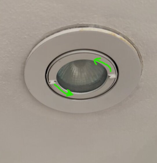 Inbyggd takspotlight i vit ram med gröna pilar som visar vridriktning för att lossa glaset.