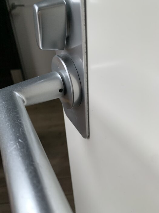 Närbild av ett dörrhandtag och lås, med en liten skruvhål synligt vid sidan av handtaget.