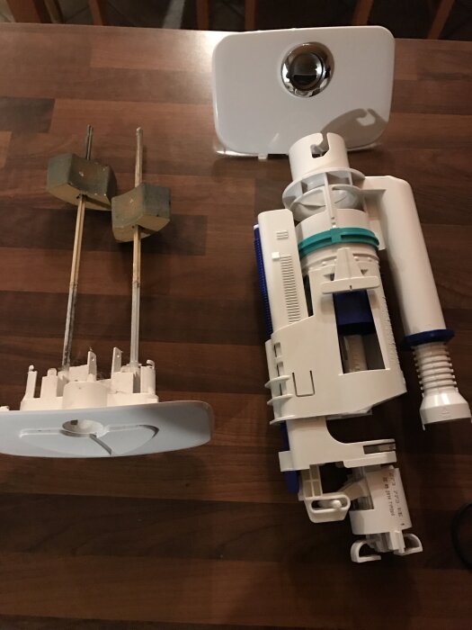 Delar av toalettens spolsystem ligger på ett träbord, inklusive två flottörer och en modern spolmekanism.