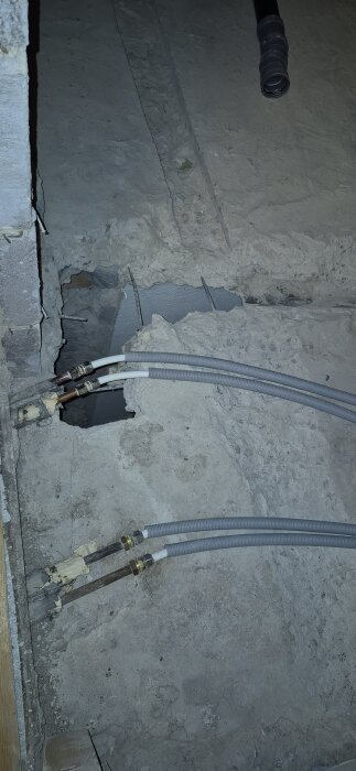 Armering och urgröpt ränna synliga i ett betonggolv, med rör och kablar intill en vägg.