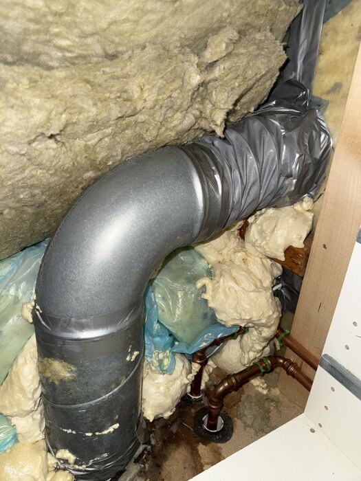 Ventilationsrör med kondens bakom borttagen byrå, dåligt isolerat i utrymme med skumisolering och synliga kopparrör.