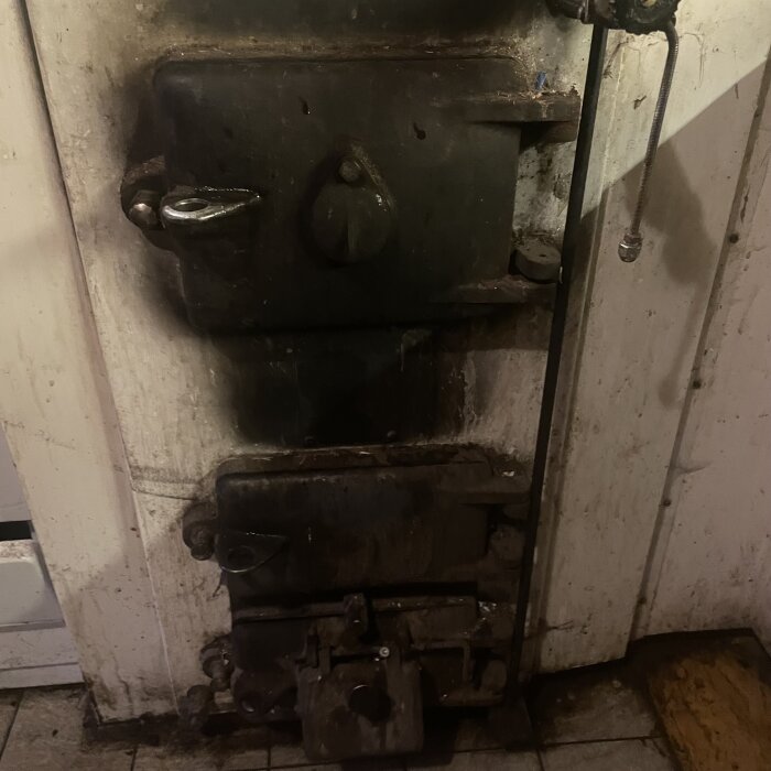 Gammal vedeldad spis med sotiga ytor och flera luckor i ett slitet kök.