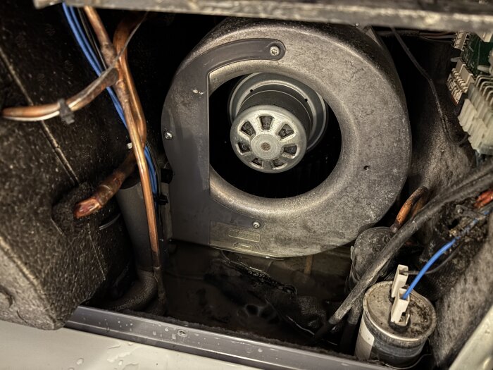 En öppning i en apparat med rör och kablar, möjligt anslutningsställe för avloppsslang som leder bort vatten, visas från insidan.