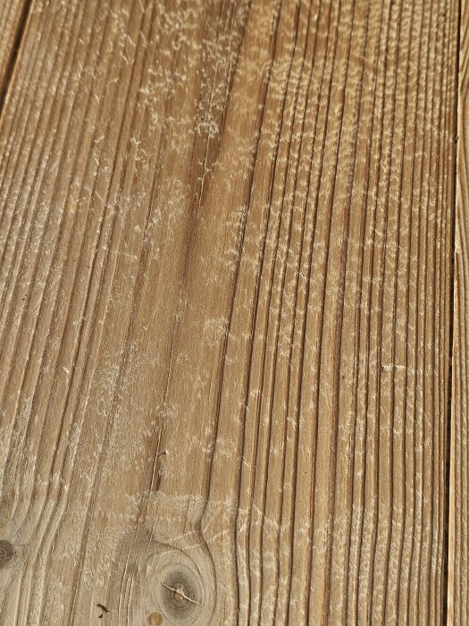 Slitet trägolv med urgröpningar och fläckar, ytan är ojämn och ruggig med synliga träfibrer, tecken på tidigare skurning med såpa.