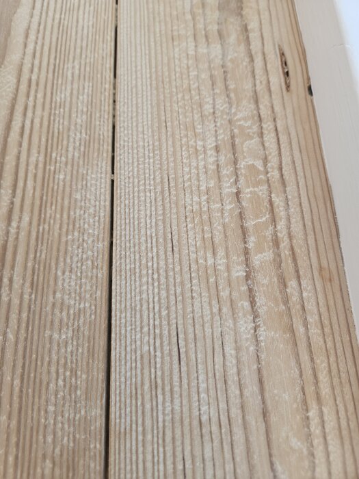 Slitet skurgolv i nära bild, visar ojämna plankor med tydliga urgröpningar och ludd av trä efter skurning.