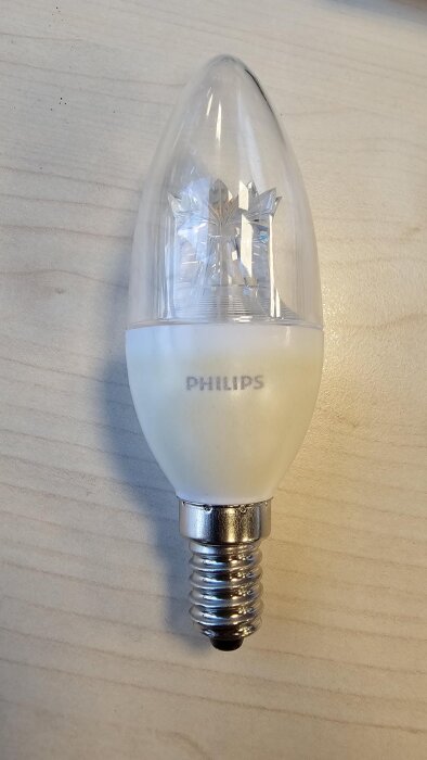LED-lampa av märket Philips med metallsockel, liggande på en träyta.