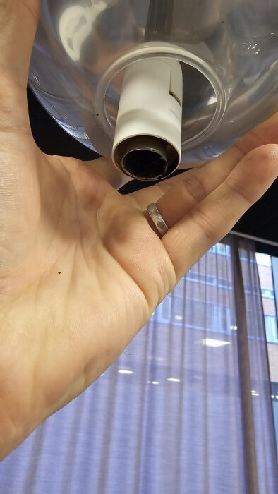 Hand håller i en lampa med en bränd sockel i en armatur, mot en bakgrund av glasfönster och gardiner.