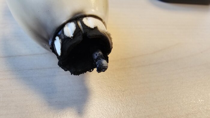 Bränd och smält lampa med metallsockeln exponerad, liggande på ett bord.