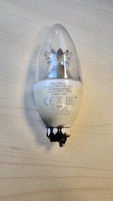 Bränd LED-lampa med metallsockel delvis skadad, liggande på träbord.