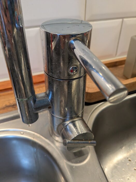 Kökskran i metall med läckage vid handtaget, fotograferad ovanifrån med en diskbänk i bakgrunden.